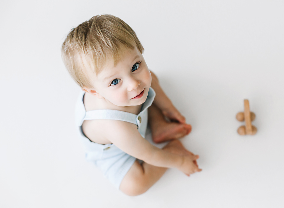 Baby boy sitting on floor in blue overalls playing with a wooden toy