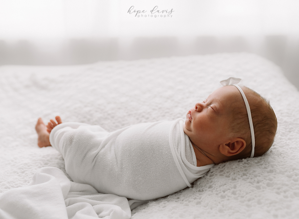 Backlighting of newborn baby girl on white. Using a raised dog bed as poser. Minimalist white newborn photography.