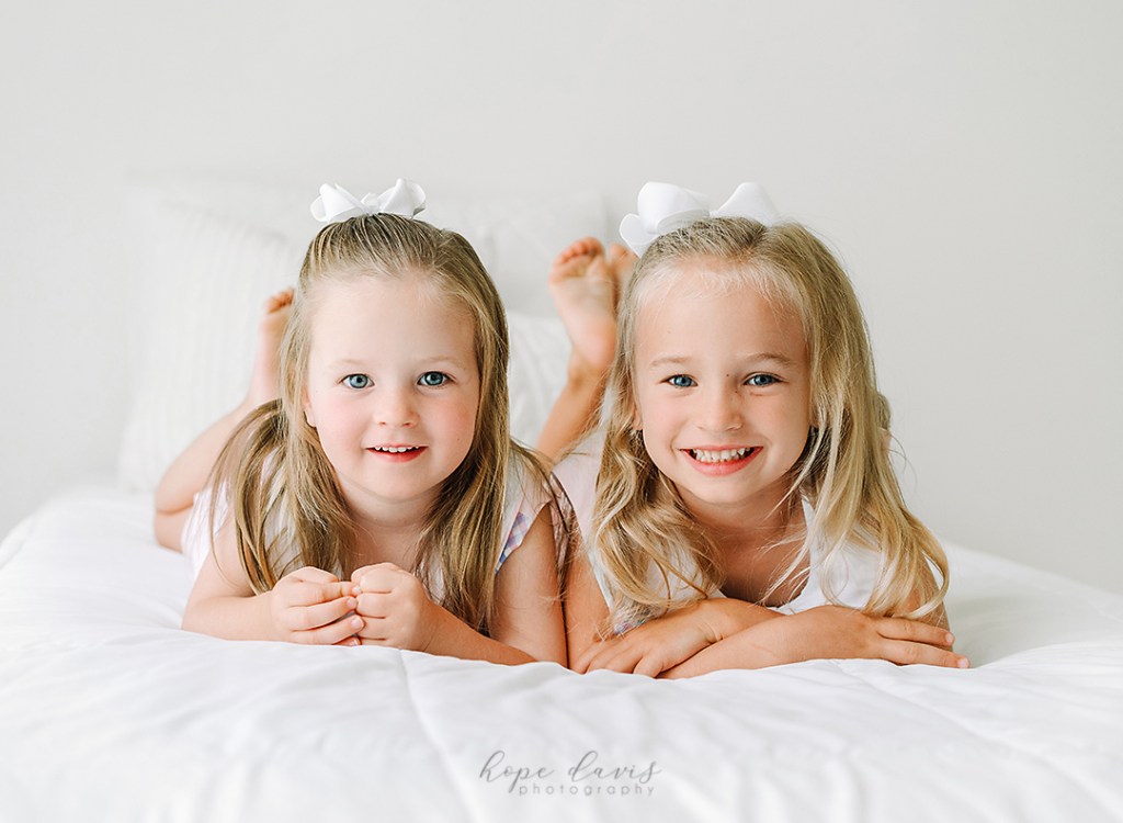 sister photo session, laying on a white bed in a white studio